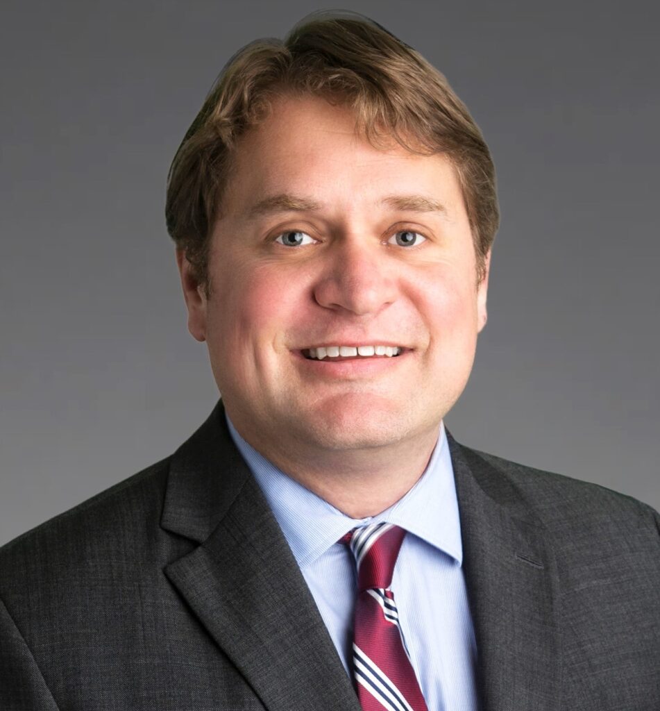 Andy Wright, a man with short, light brown hair wearing a gray suit jacket and red and white tie.